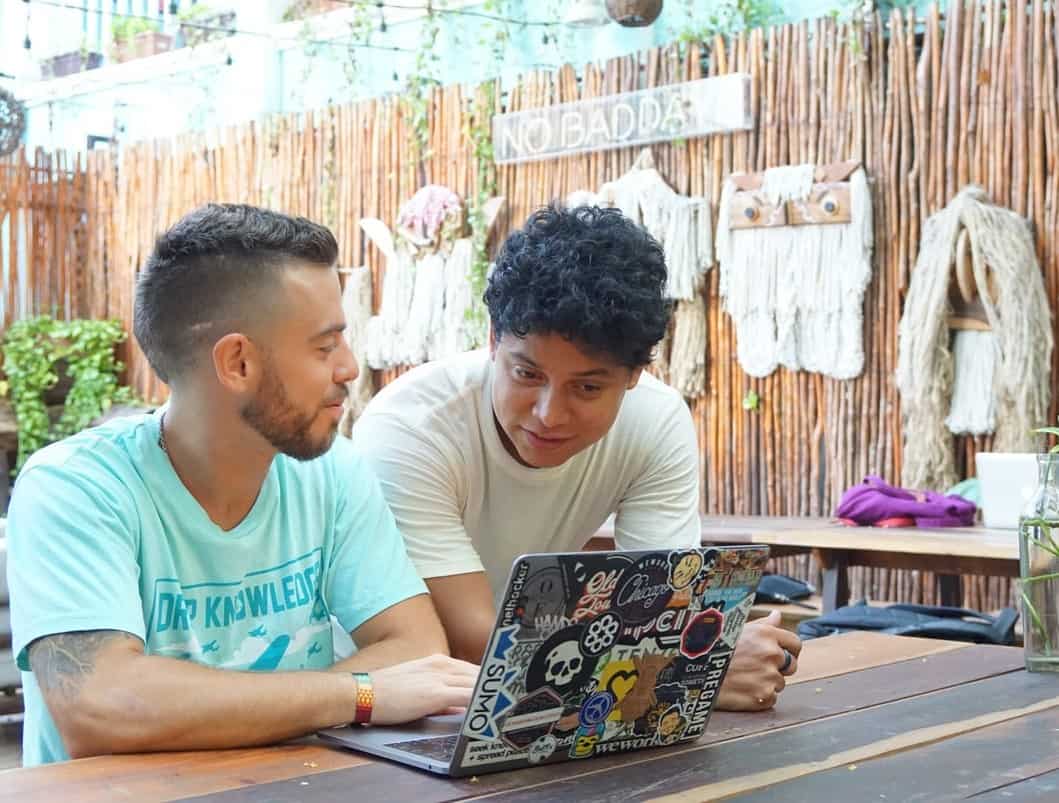 Two men look at a laptop together while talking and smiling